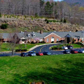 Aerial view of a building surrounded by green grass and trees, with several cars parked in the lot.