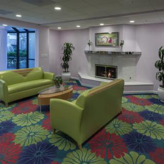 A cozy lobby area with green couches, vibrant floral carpet, and a fireplace.