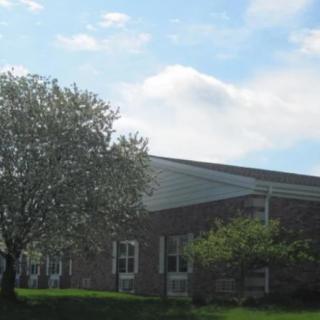 A brick building with adjacent trees under a partly cloudy sky.