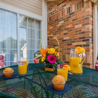 A cozy outdoor breakfast setup with orange juice and muffins on a patio table, complemented by a vibrant flower arrangement.