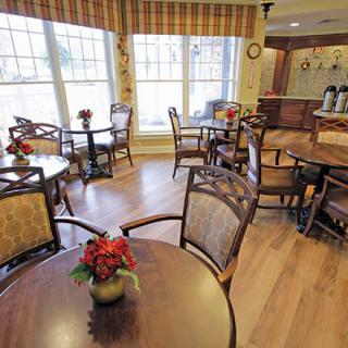 A cozy cafe interior with wooden tables and chairs, adorned with floral decorations near large windows.