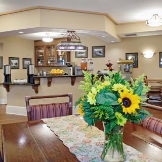 A cozy dining area with a table adorned by a bouquet of sunflowers, leading to a well-equipped kitchen in the background.