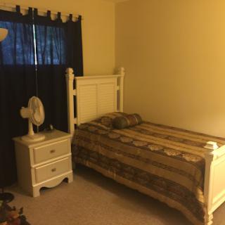 A simple and cozy bedroom setup featuring a bed, nightstand, and fan.