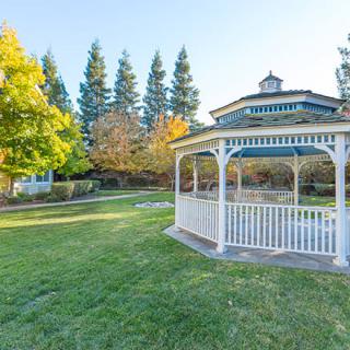 A scenic view of a park with a white gazebo, surrounded by grass and autumn trees.