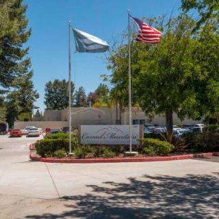 A parking lot entrance with American and company flags, surrounded by trees.