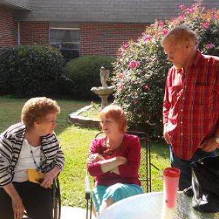 A group of three people engaged in conversation outdoors, enjoying a sunny day in the garden.