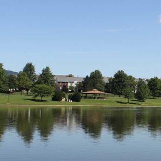 A serene park setting with a lake reflecting surrounding trees and a distant building.
