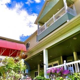 A two-story house featuring balconies and a vibrant garden under a blue sky.