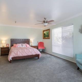 A spacious bedroom with modern decor, featuring a bed, chairs, and large windows.