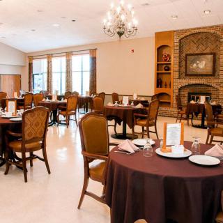 An elegant dining room featuring neatly arranged tables and chairs, with large windows and a cozy fireplace.