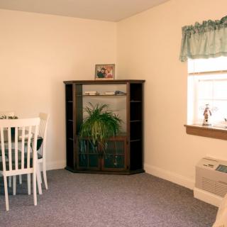 A cozy room with a dining area, featuring a corner shelf and window.