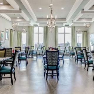 An elegantly designed dining room with multiple tables and chairs, featuring chandeliers and large windows with curtains.