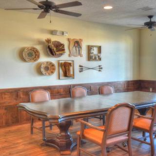 A stylish dining room with a large wooden table, cushioned chairs, decorative wall art, and ceiling fans.
