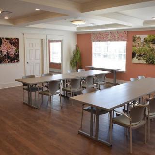 A modern conference room with tables and chairs arranged for a meeting, featuring wood flooring and decorative artwork on the walls.