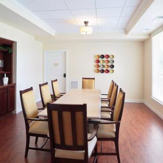 A well-lit dining room with a long table and several chairs, featuring wooden flooring and modern wall art.