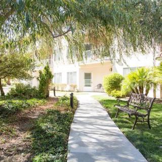A serene garden pathway lined with trees and a bench, leading to a building in the background.
