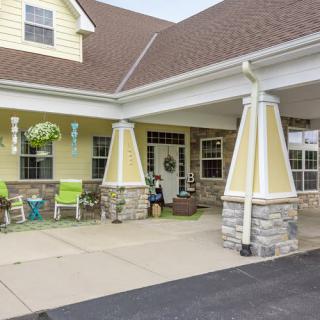 A welcoming porch with columns and stonework, featuring seating and hanging plants.