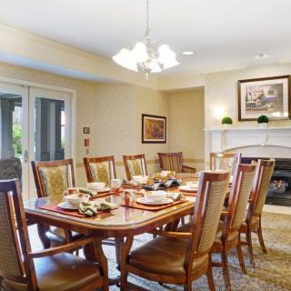 A spacious dining room with a long wooden table and elegant chairs, featuring a chandelier and a fireplace.