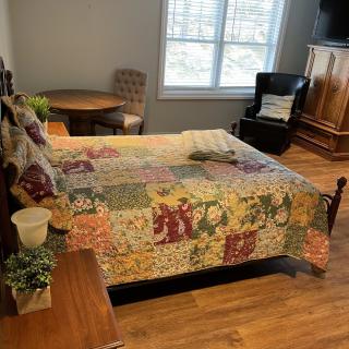 A cozy bedroom featuring a colorful quilt on the bed, with hardwood flooring and classic furniture.