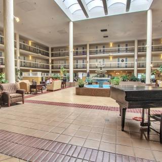 A spacious hotel lobby featuring a piano and comfortable seating under a skylight.