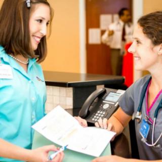 A nurse and a patient interacting at the reception desk in a healthcare setting.