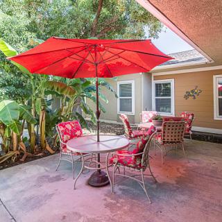 A cozy outdoor patio with a red umbrella, surrounded by lush greenery.