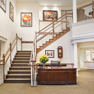 A spacious lobby with a wooden reception desk and a grand staircase adorned with artwork.