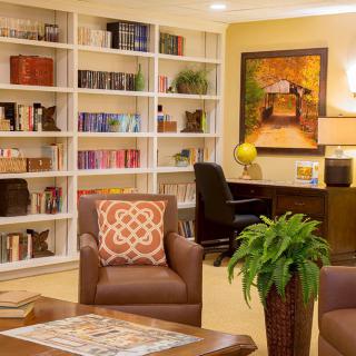 Cozy library lounge with bookshelves, armchairs, and a desk area.