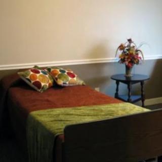A simple bedroom with a bed, colorful pillows, and a small table with a flower vase.