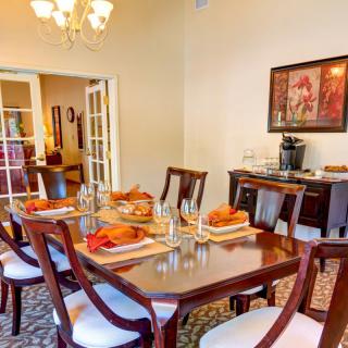 An elegantly set dining room with a polished wooden table and chairs, adorned with a chandelier and decorative artwork.