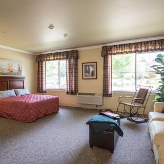 A cozy hotel room featuring a bed, an armchair, and large windows with patterned curtains.