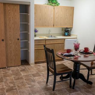 A cozy kitchen and dining area featuring wooden cabinets, a small round table set with dishware, and a pantry with sliding doors.