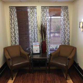 A cozy waiting area featuring two brown chairs, a small table, and decorative elements.