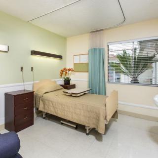 A clean and well-organized hospital room with a single bed and natural lighting.