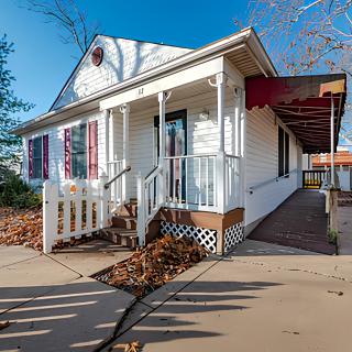 A small white house with a porch and a ramp, surrounded by fallen leaves on an autumn day.
