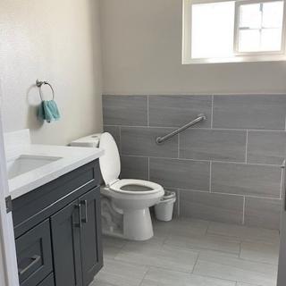 A modern bathroom with a toilet, sink, and handrail under a small window.