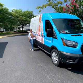 A woman standing next to a blue delivery van on a sunny day.