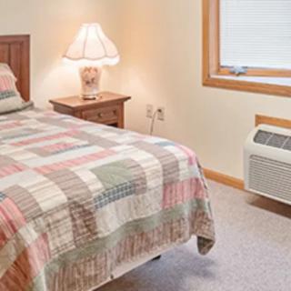 A cozy bedroom with a single bed, bedside lamp, and a quilted bedspread.