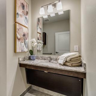 A modern bathroom with a sleek countertop, featuring a mirror, floral decor, and neatly folded towels.