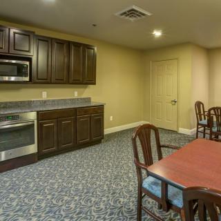 A view of a carpeted kitchen and dining area with wooden cabinets, a microwave, and a table with chairs.