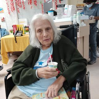 An elderly woman enjoying a snack while seated in her wheelchair.