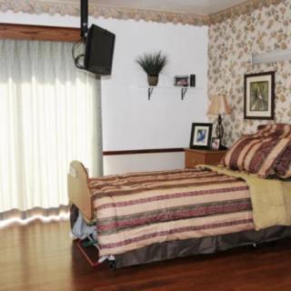 A cozy bedroom with floral wallpaper, a striped bedspread, and a wall-mounted TV.