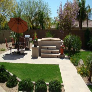 A well-landscaped backyard features a patio with outdoor seating, an umbrella, and a barbecue grill.