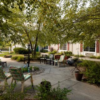 A tranquil garden patio with seating under leafy trees.