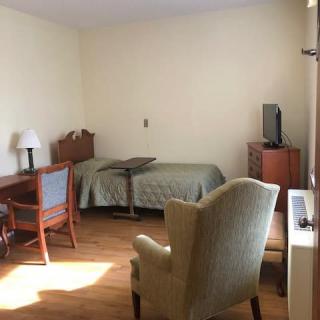A simple bedroom with a single bed, a desk, and a television.