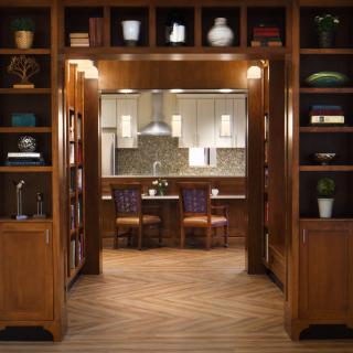 A cozy kitchen viewed through a room lined with wooden bookshelves.