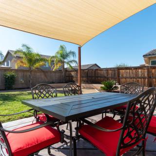 A sunny backyard patio with a table and chairs under a shade sail.