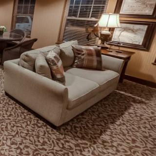 A cozy living room scene featuring a comfortable sofa with patterned cushions, a warm lamp on a side table, and framed artwork on the walls.