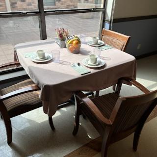 A neatly arranged dining table by the window, adorned with a fruit centerpiece.