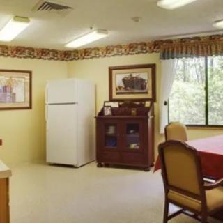 A cozy kitchen and dining area with a refrigerator, wooden table, chairs, and artwork on the walls.